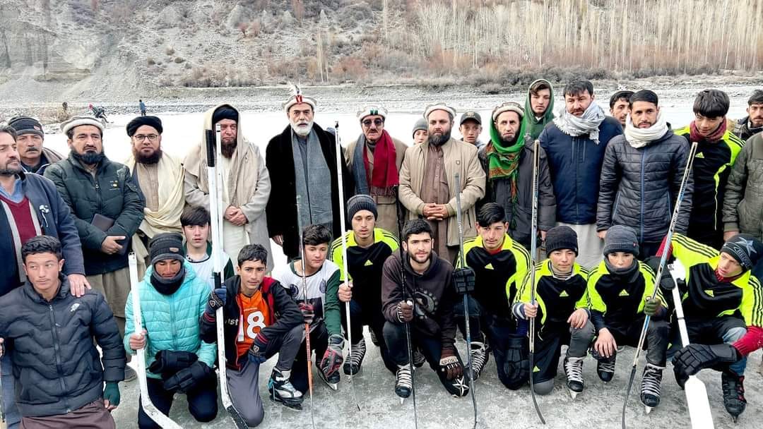 Youth and adults with hockey sticks on frozen river in mountain valley