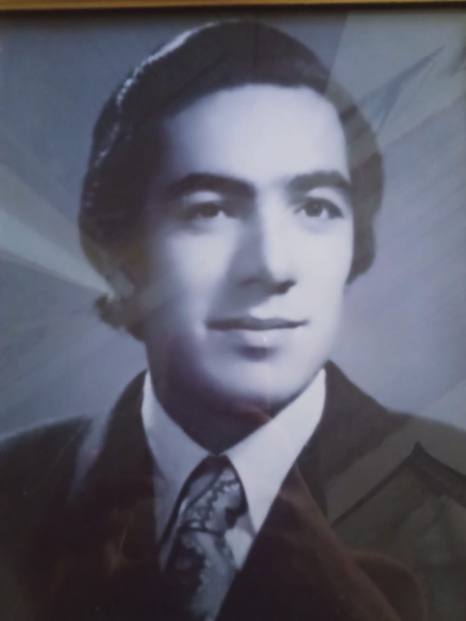 Vintage black-and-white portrait of a young man from Chitral wearing traditional cap and western suit