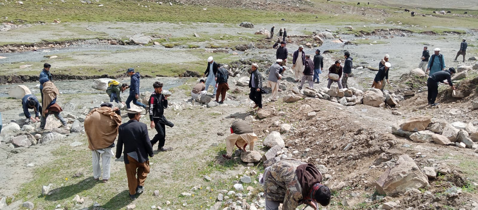 Community members working together to build stone structures along a mountain stream