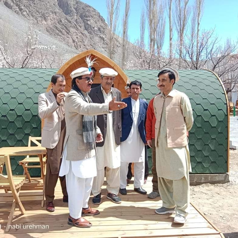 Community members visiting a tourism glamping site in Chitral with mountains and cherry blossoms
